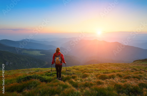 Sporty girl with back sack is standing at the lawn and watching on the endless cast of mountains landscape.