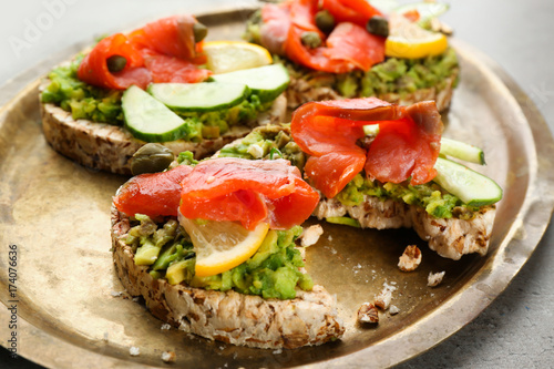 Tasty crispbread sandwiches with salmon and avocado on metal dish