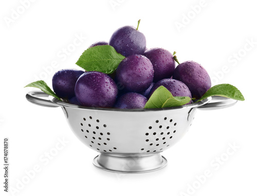 Colander with ripe plums on white background