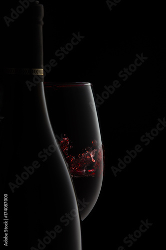 A bottle and glass of elegant red wine with splash.