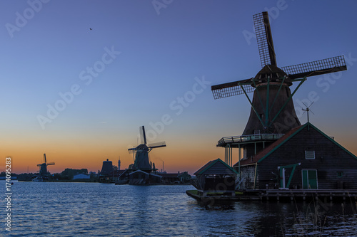 Travel Ideas. Amazing Picturesque View of traditional Dutch Windmills At Sunset During Golden Hour in Zaanse Schans near Amsterdam.