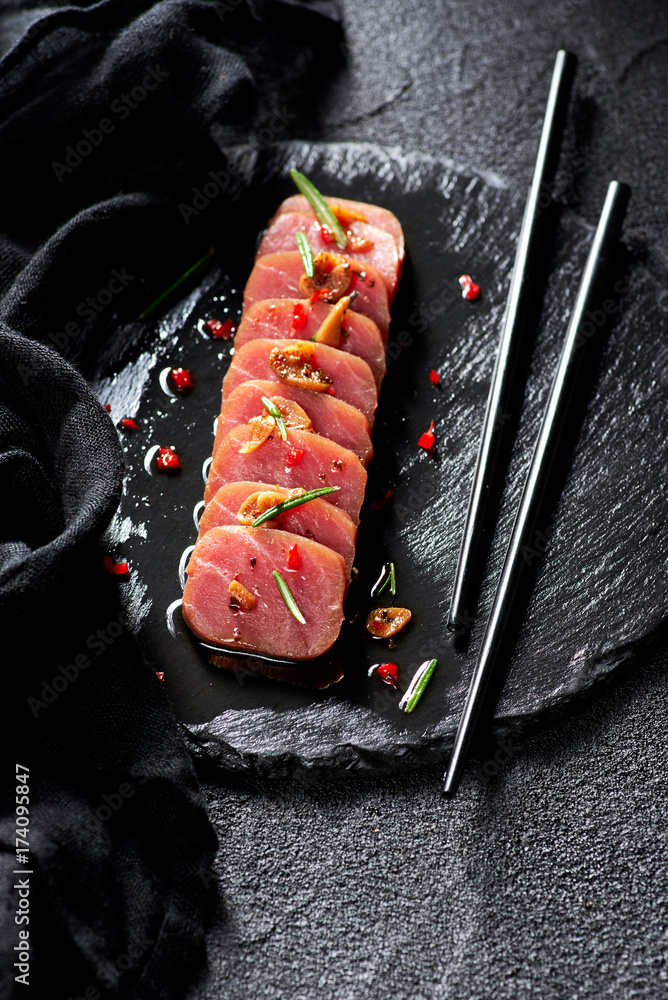 Tuna steak in oil with chilli and rosemary on black slate plate