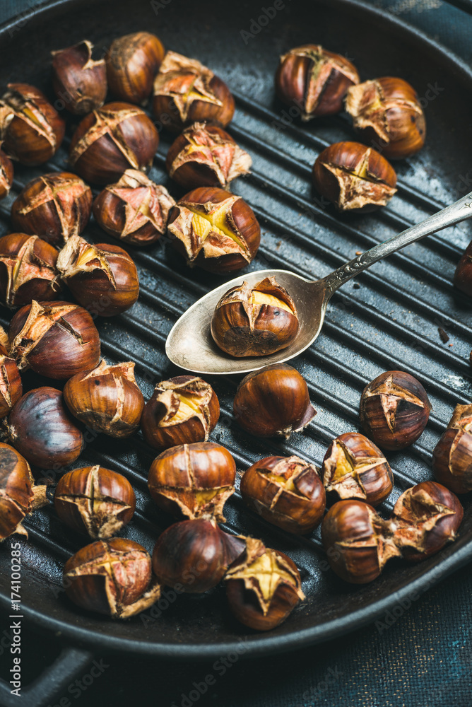 Close-up of roasted chestnuts in cast iron grilling pan over dark blue shabby plywood background, top view, selective focus, vertical composition Close-up of roasted chestnuts in cast iron grilling pan over dark blue shabby plywood background, top view, selective focus, vertical composition