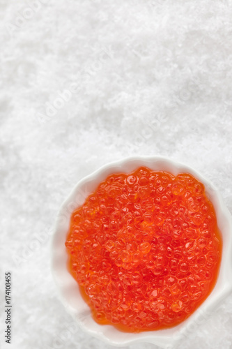 Delicious red caviar in bowl on white snow background photo