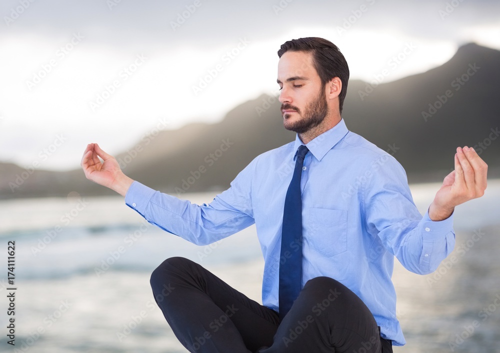 Business man meditating against blurry coastline Business man meditating against blurry coastline