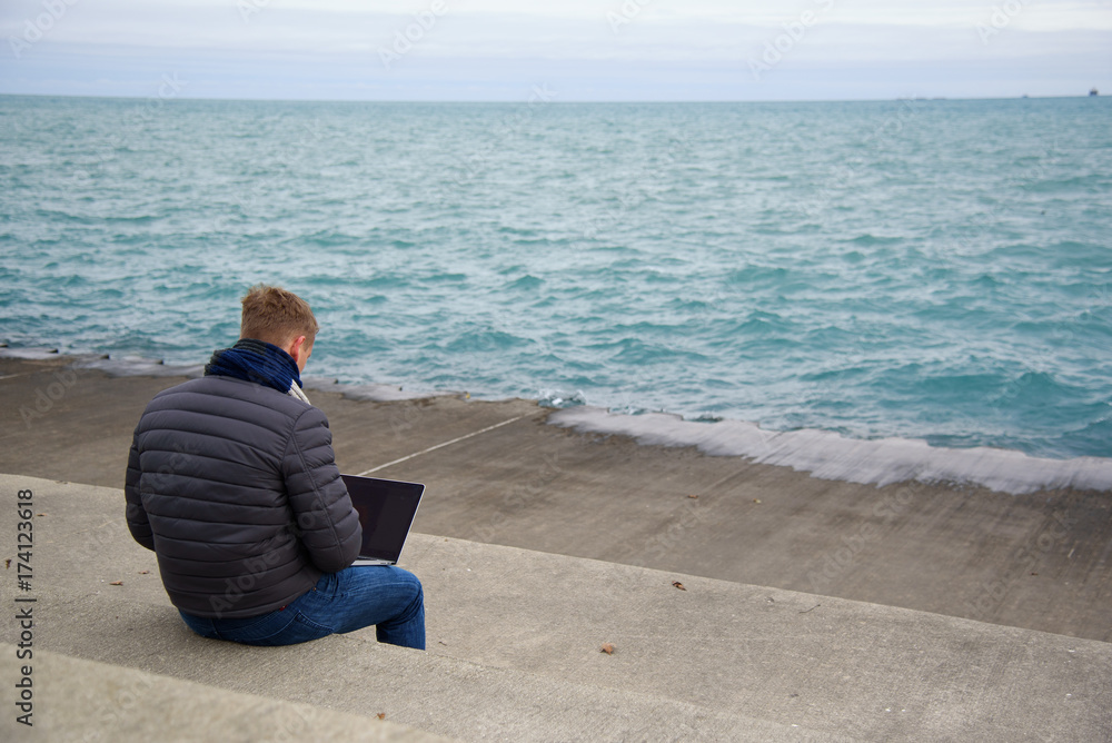 A young man is working on the sidewalk near lake