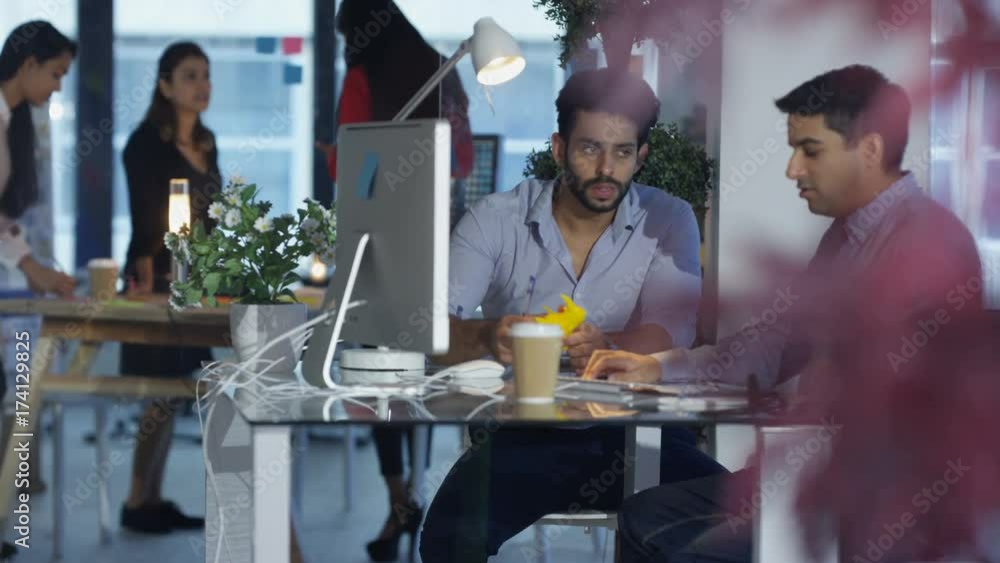 Designers at desk with colleagues working in background. Designers at desk with colleagues working in background.