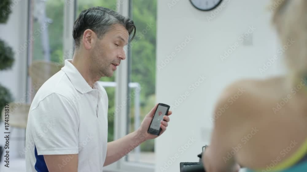  Fitness trainer using smartphone app to train mature female client 