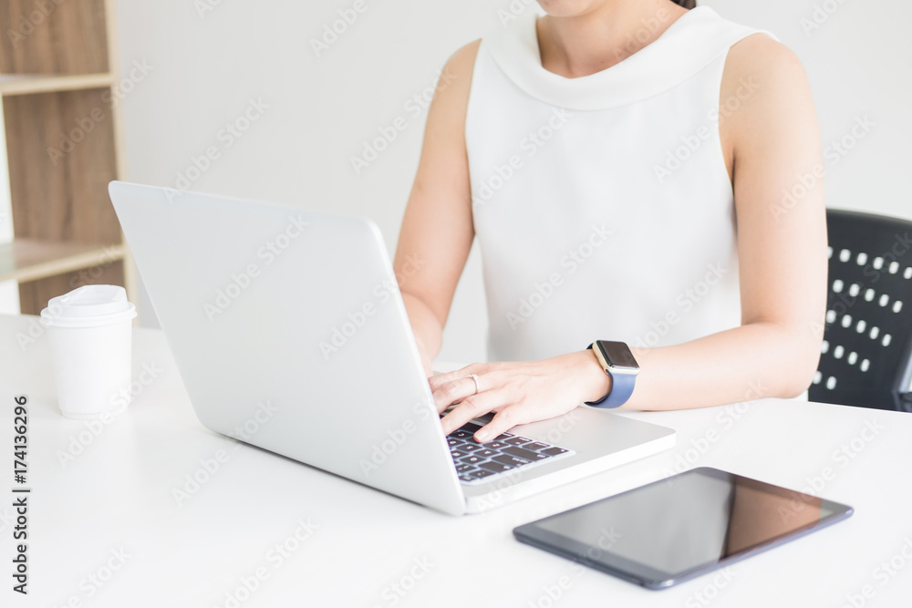 Fototapeta premium Attractive women in casual business sitting at a table working on her laptop computer at home office in front of a window.