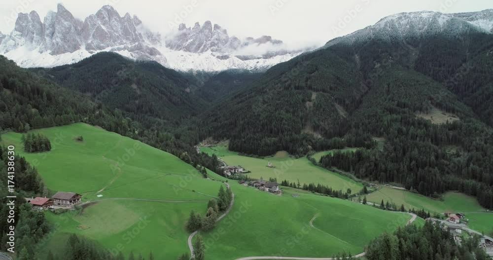 Amazing aerial shot of Dolomiti mountain on a cloudy autumn day. Flying above beautiful green forest in Santa Maddalena in Val di Funes, Dolomites, Italy with view over Italian Alps. Amazing aerial shot of Dolomiti mountain on a cloudy autumn day. Flying above beautiful green forest in Santa Maddalena in Val di Funes, Dolomites, Italy with view over Italian Alps.