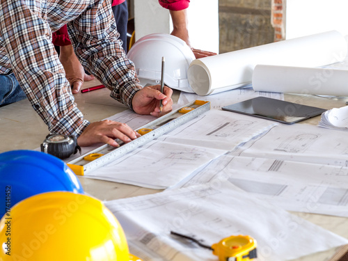 Engineer/architect/worker man discussing about building plan for construction at job site, working on desk/table with drawing/blueprint/business plan