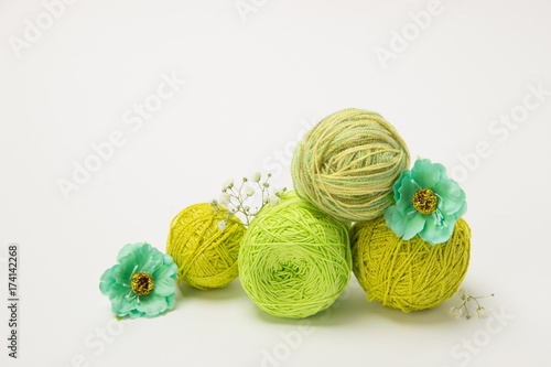 Green thread for knitting in tangles and needles with flowers on a white background