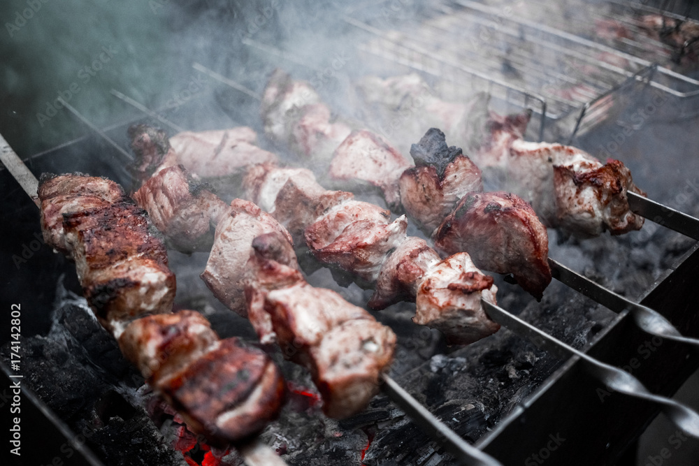 Grilled kebab cooking on metal skewers (grill). Roasted meat cooked at barbecue with smoke. Close up BBQ fresh pork meat chop slices. Traditional eastern dish, shish kebab.