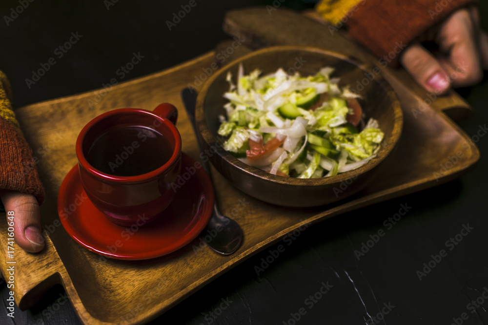 Man holding wooden tray with a salad and coffee on a black background Man holding wooden tray with a salad and coffee on a black background
