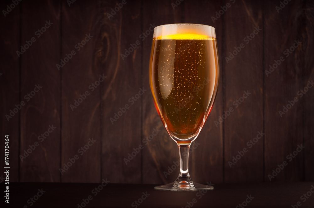 Goblet beer glass with golden sparkling lager on dark wood board, copy space. Template for advertising, design, branding identity, restaurant menu, cover. Goblet beer glass with golden sparkling lager on dark wood board, copy space. Template for advertising, design, branding identity, restaurant menu, cover.