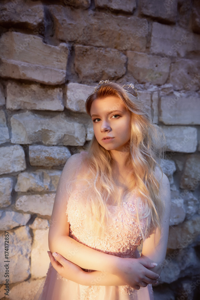 Portrait of a beautiful bride blond girl in pink lace dress ,hair decoration, handmade. Tenderness. Standing amid the old walls of stones, manual clutch. Hard interesting sunset color
