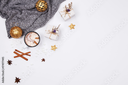 Winter christmas holiday background. Cup of hot chocolate drink with marshmallows, cinnamon sticks, anise star, gift box and golden ornaments on white background.