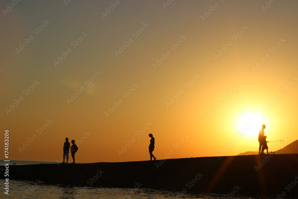 Fototapeta premium silhouette of people in the sun, sunset, silhouettes of people on the pier, evening walk