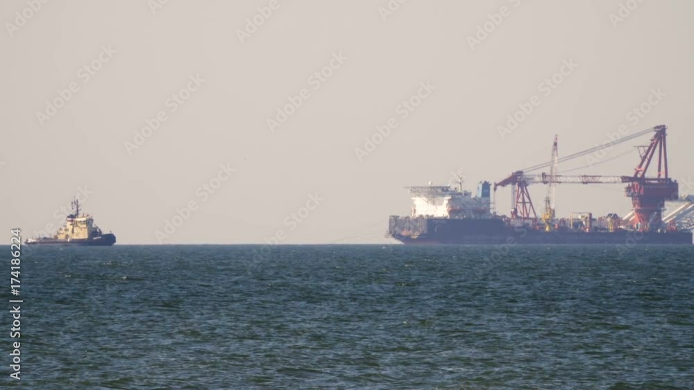 Cargo freighter ship sailing, moving at ocean horizon sky in hazy sea. Multi-purpose vessel carrying bulk cargo on deck across sea. Shipping services Cargo freighter ship sailing, moving at ocean horizon sky in hazy sea. Multi-purpose vessel carrying bulk cargo on deck across sea. Shipping services