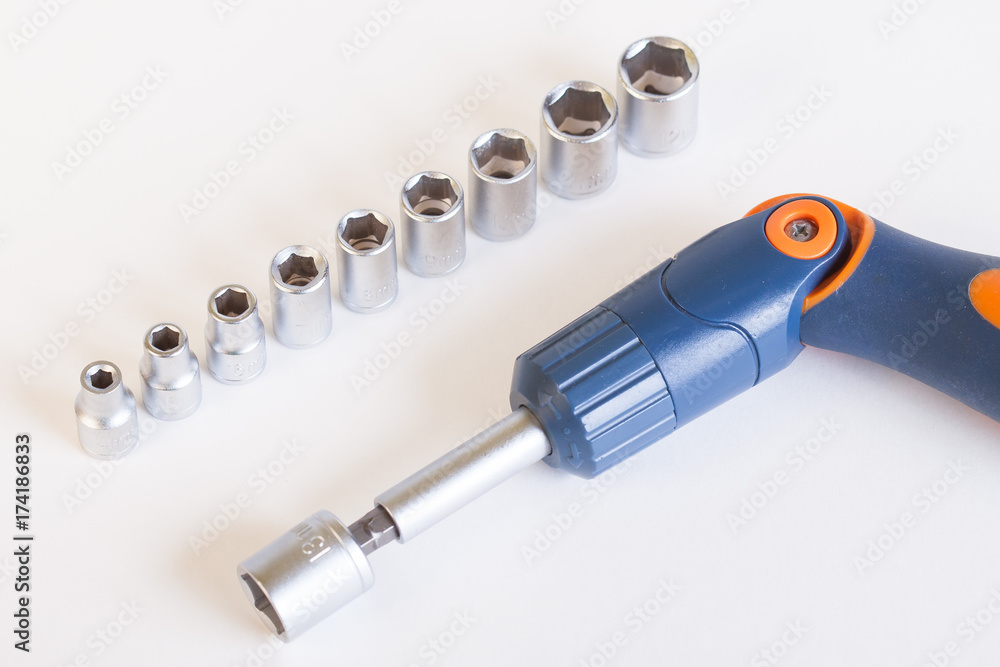 Top view of the screwdriver head. A set of heads and a screwdriver on a light background. Screwdriver with blue - orange bent handle and a set of heads under the nut. Top view of the screwdriver head. A set of heads and a screwdriver on a light background. Screwdriver with blue - orange bent handle and a set of heads under the nut.