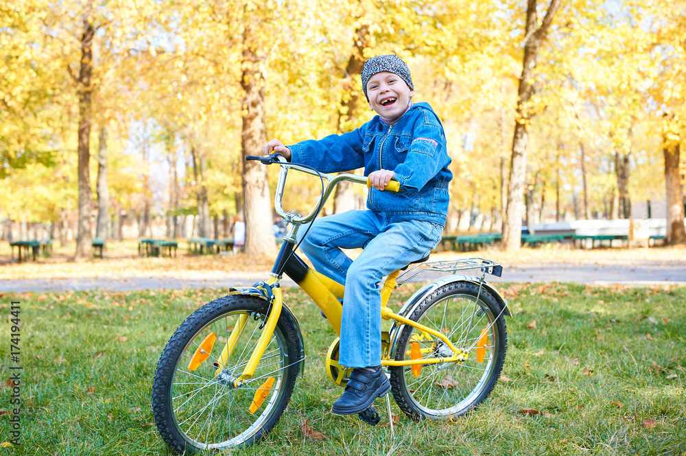 boy riding on Bicycle in autumn Park, bright sunny day, fallen leaves on background