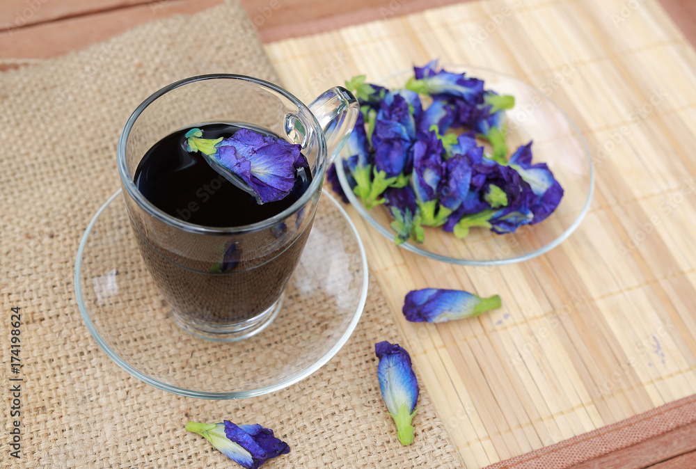 Butterfly pea juice in transparent glass and flowers on sack - wood mat background. Butterfly pea juice in transparent glass and flowers on sack - wood mat background.