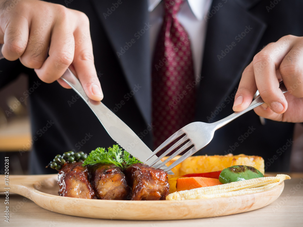 Businessman holding fork and knife eating steak, business and food concept