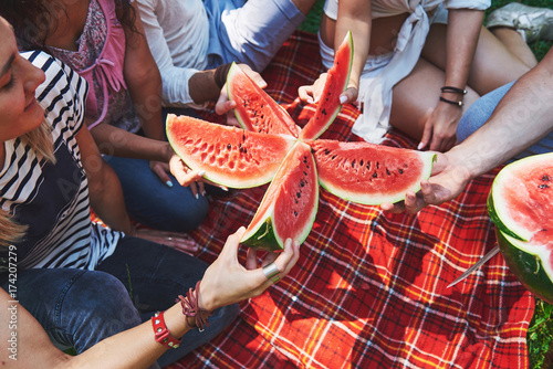 Cheerful friends enjoying watermelon on picnic on sunny summer day photo