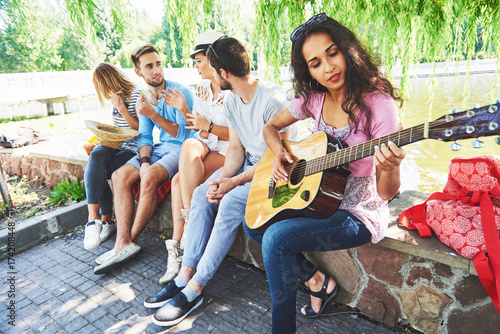 Group of happy friends with guitar. While one of them is playing guitar and others are giving him a round of applause photo