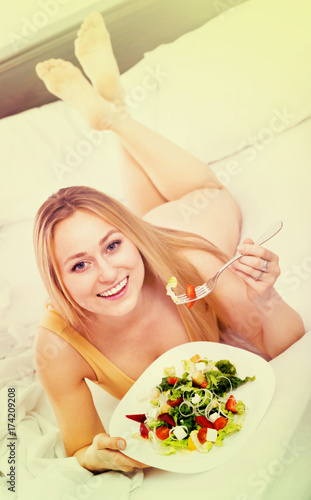 Blond woman in underwear sitting in the bed and enjoying a salad