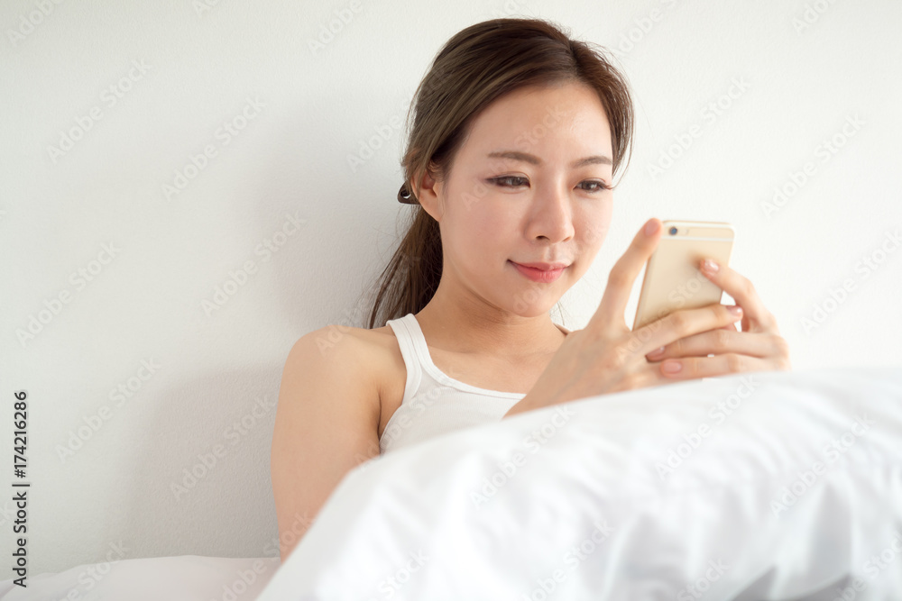 Young asian woman wake up happy, using smart phone reading good news on the bed with fresh feeling in the morning Young asian woman wake up happy, using smart phone reading good news on the bed with fresh feeling in the morning