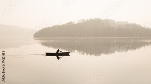 Foggy day.  A man is swimming in a boat.