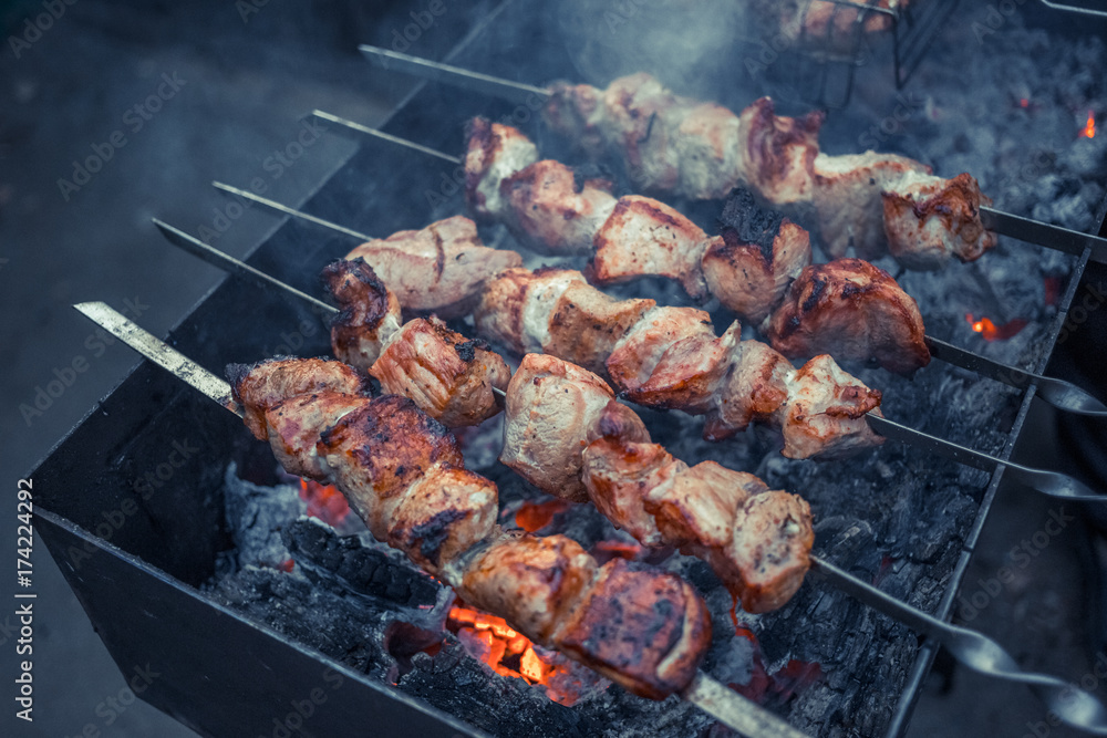 Grilled kebab cooking on metal skewers (grill). Roasted meat cooked at barbecue with smoke. Close up BBQ fresh pork meat chop slices. Traditional eastern dish, shish kebab Grilled kebab cooking on metal skewers (grill). Roasted meat cooked at barbecue with smoke. Close up BBQ fresh pork meat chop slices. Traditional eastern dish, shish kebab