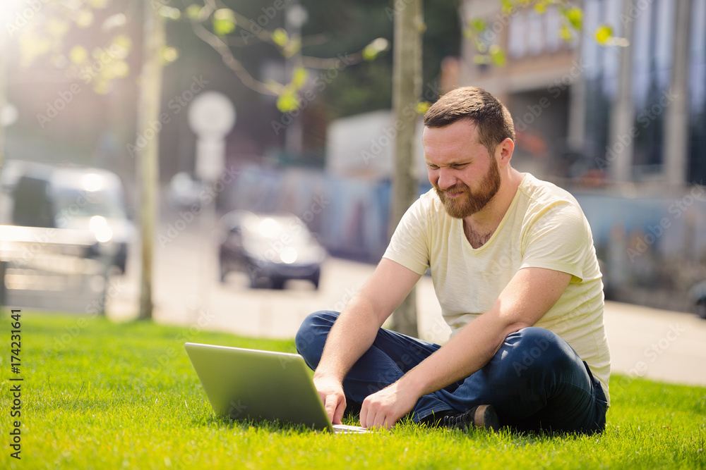 Obraz premium young man with a laptop on the lawn, working outdoors in the city