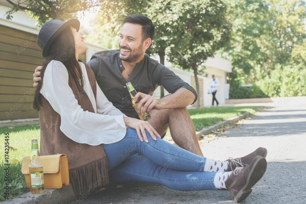 Young couple sitting in park and holding bottle of drink.