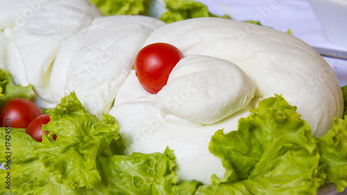 Dettaglio di una treccia enorme di mozzarella di bufala campana. Il prodotto caseario e steso su un letto di lattuga e decorato con pomodini rossi del Vesuvio. Il prodotto è in esposizione. photo