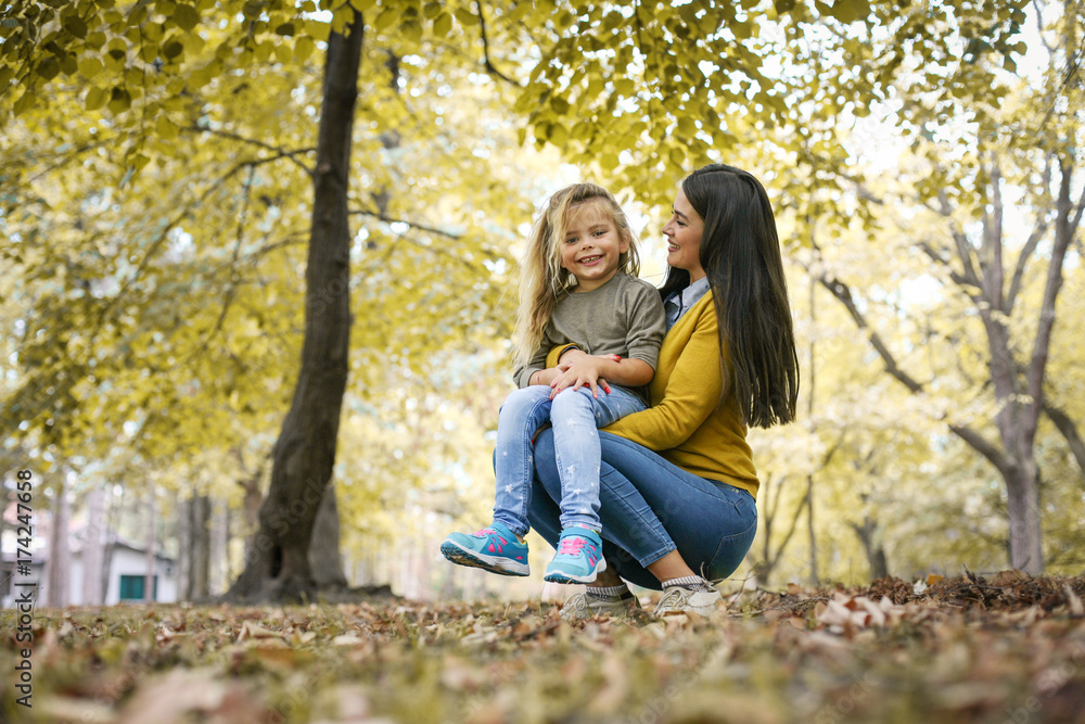 Fototapeta premium Mother and daughter outdoors in a meadow. Little girl sitting on mother lap.