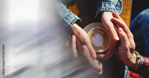 Overhead of two pairs of hands around coffee cup with heart in