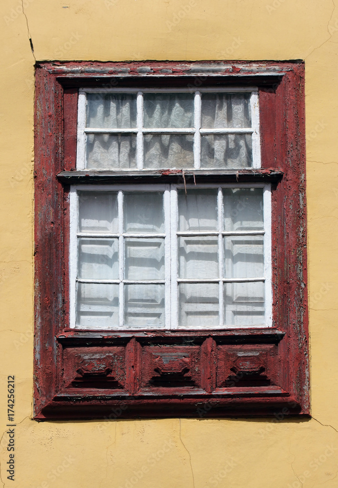 old red painted window frame with white borers on small panes of glass internal white shutters and yellow cracked wall
