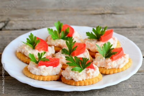 Salty crackers with cream cheese on a serving plate. Simple snack from salted crackers, savory cream cheese, fresh tomato slices and parsley. Healthy homemade snack photo. Closeup