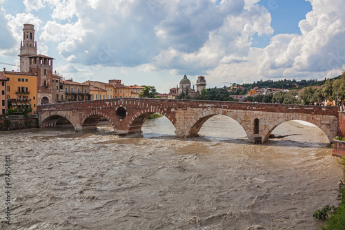 Ancient stone bridge Ponte Pietra and the turbulent River Adige in Verona in cloudy summer day, Italy