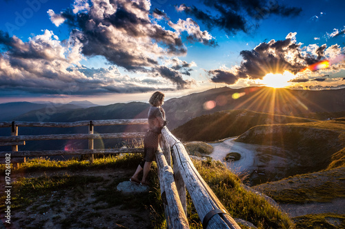 Girl leaning against the fence watching a beautiful sunset in a peaceful and tranquil place, Mount Pizzoc summit, Veneto, Italy photo