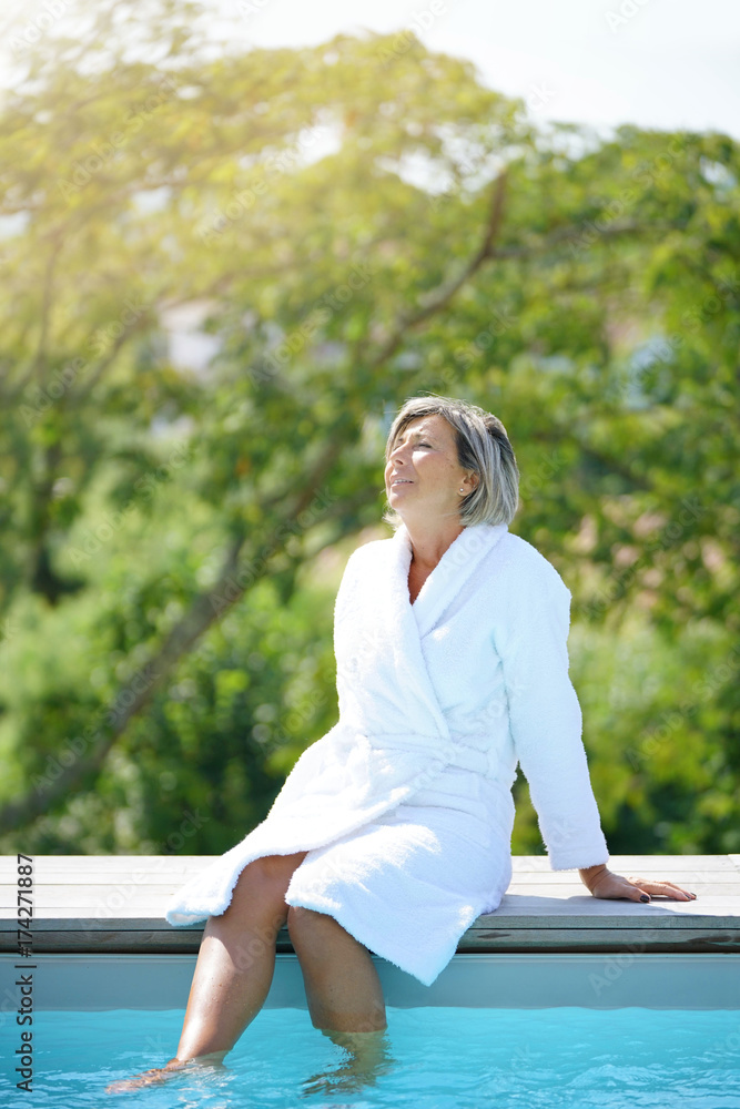Senior woman with bathrobe relaxing by swimming-pool