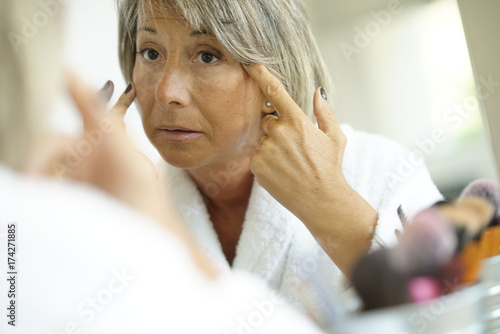 Senior woman in front of mirror looking at her skin and wrinkles