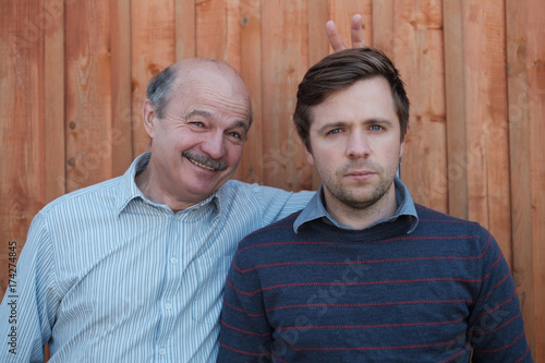 Father pranking his son with bunny ears isolated on wooden background. photo