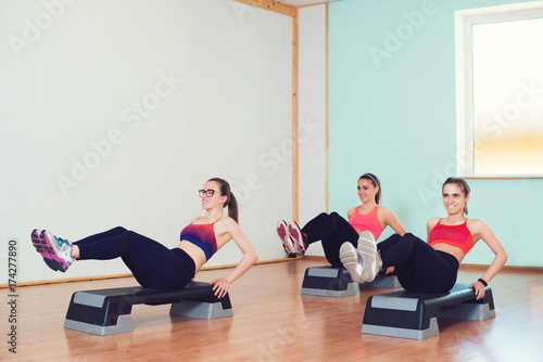 Group of young sport women working out with steppers in gym.