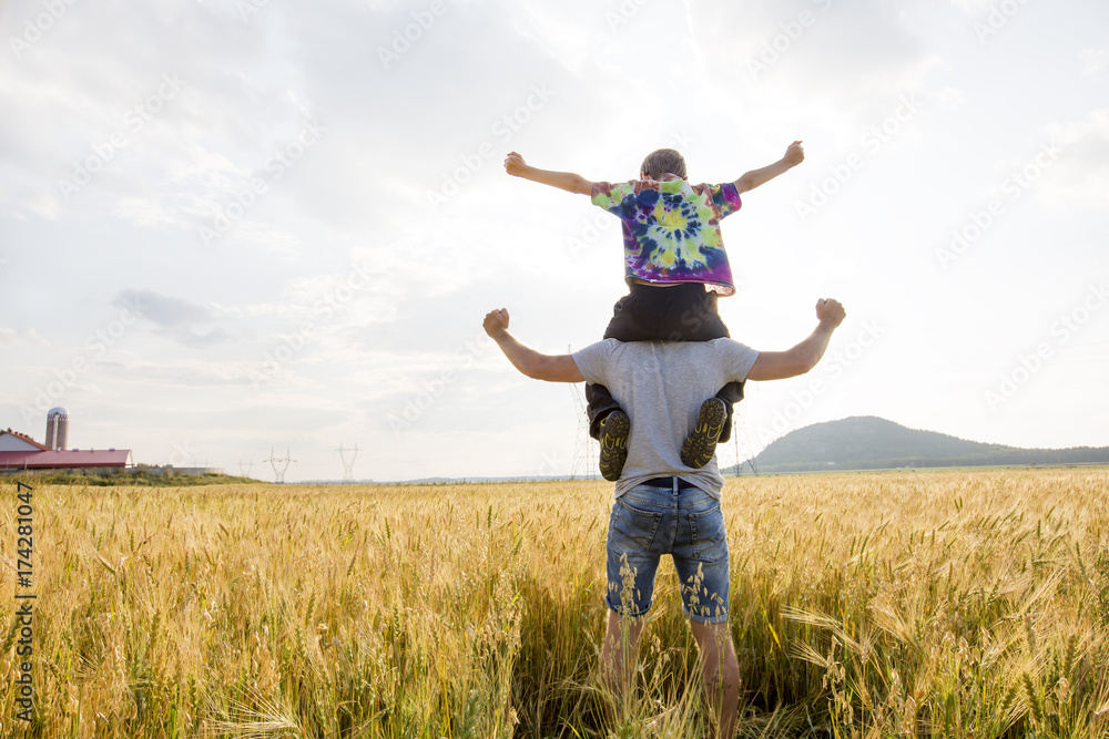 young father with his little son walking in the wheat field at sunset in a warm summer day young father with his little son walking in the wheat field at sunset in a warm summer day