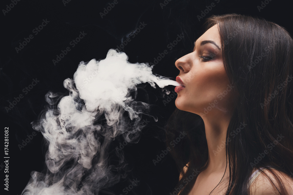 Young woman vaping e-cigarette with smoke on black closeup