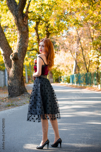 Charming redhead lady in vintage skirt and red velvet top. Stylish woman in autumn garden, pretty girl in retro doll style 