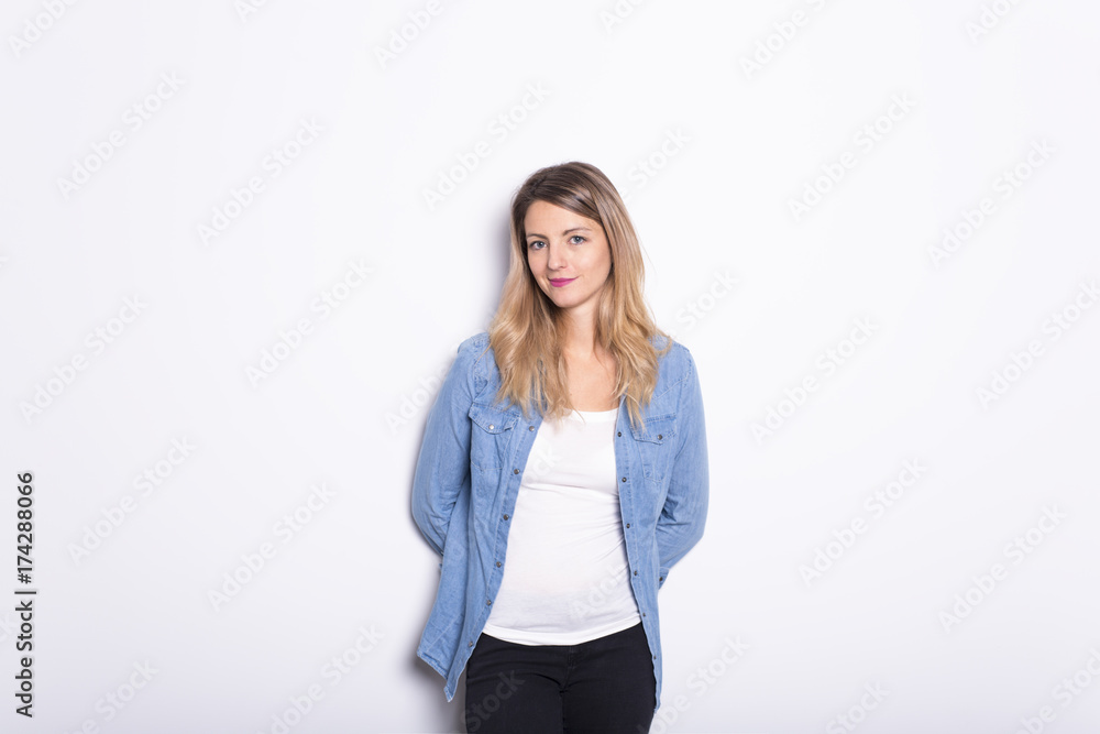 Young Woman in Denim Shirt and Jeans, Leaning Against Gray Wall Background Young Woman in Denim Shirt and Jeans, Leaning Against Gray Wall Background
